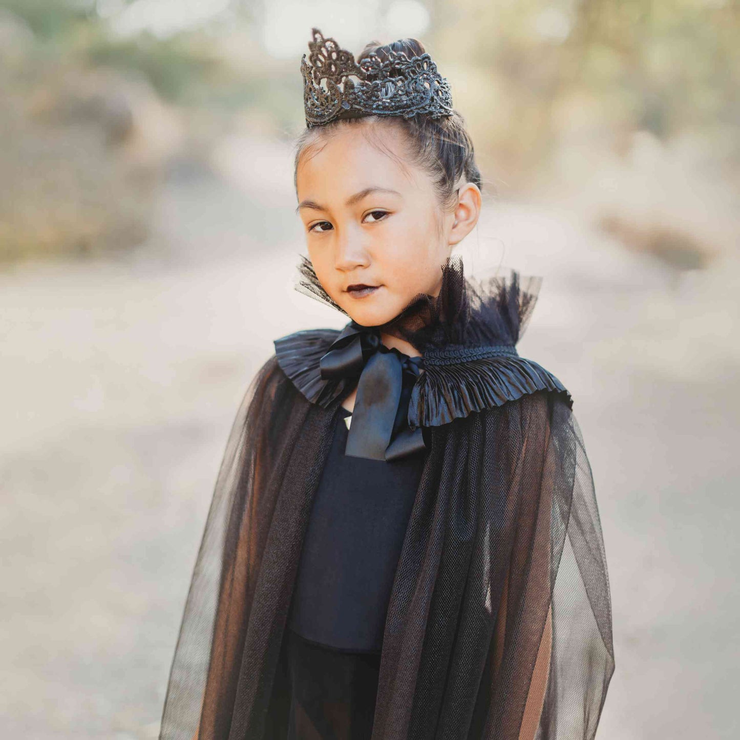a little girl wearing a black cape and a tiara