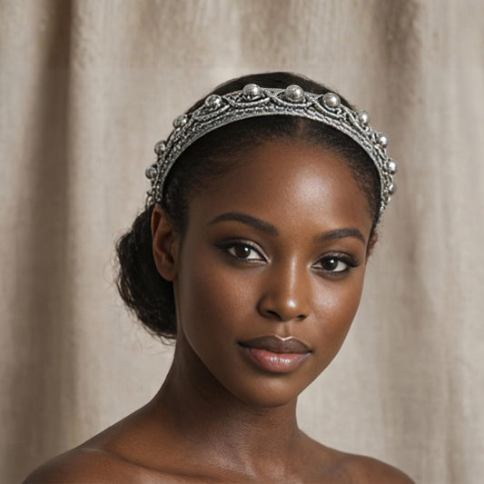 A close-up portrait of a woman wearing a silver headband with decorative elements.