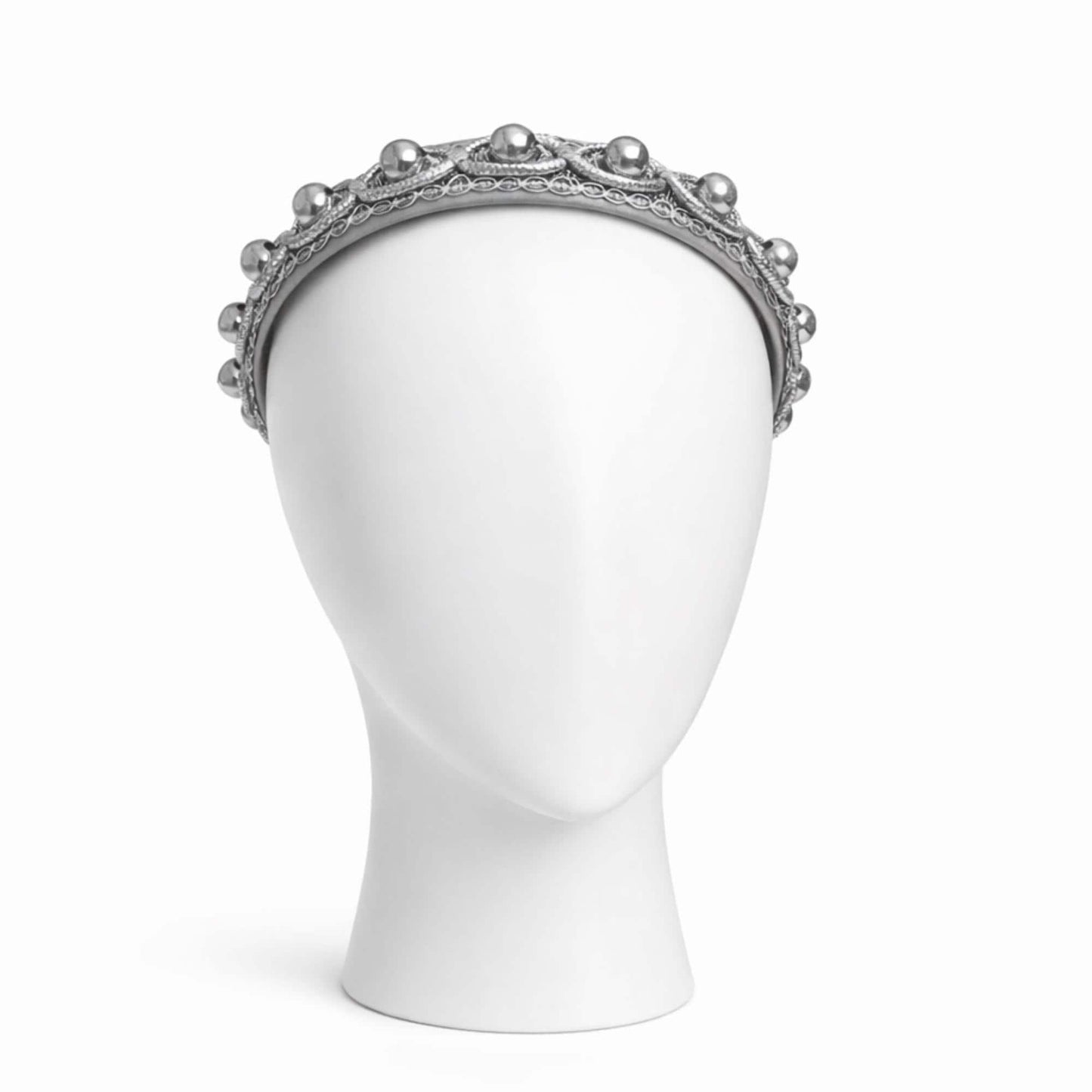 A white mannequin head wearing a silver headband with a decorative design.