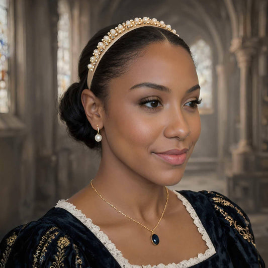 A woman wearing a gold headband and a necklace with a blue stone pendant, posing in a room with arched windows.