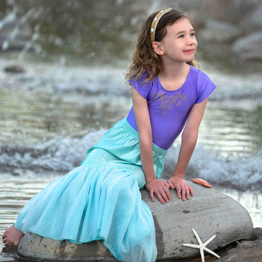 a little girl sitting on a rock in the water