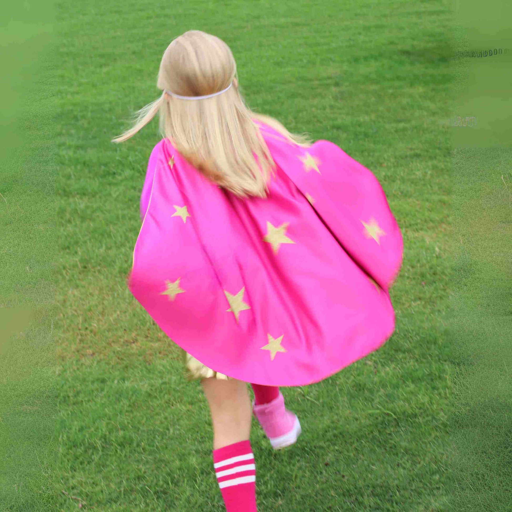 a little girl in a pink cape walking across a field