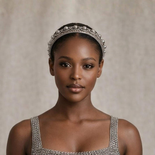 A woman wearing a silver headband and a silver dress stands against a plain background.
