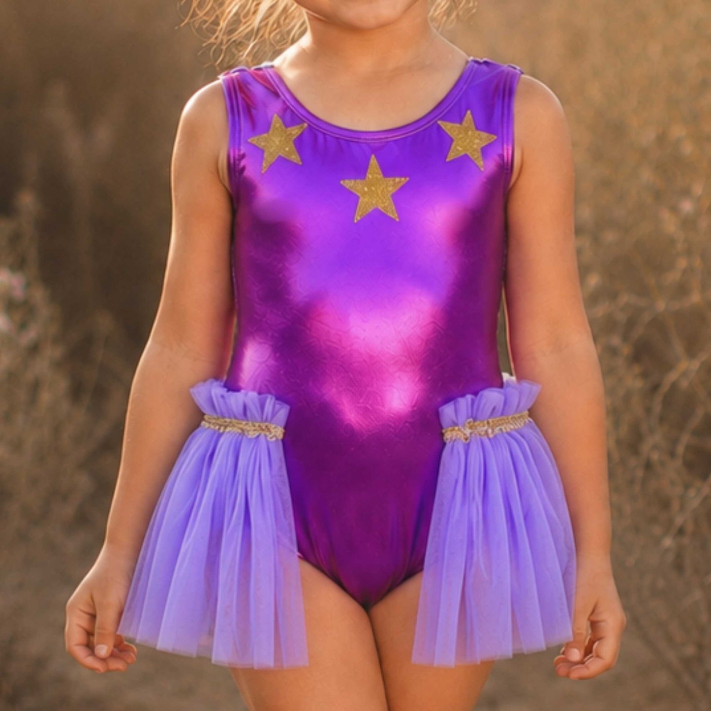 A young girl wearing a purple leotard with gold stars and a tulle skirt.