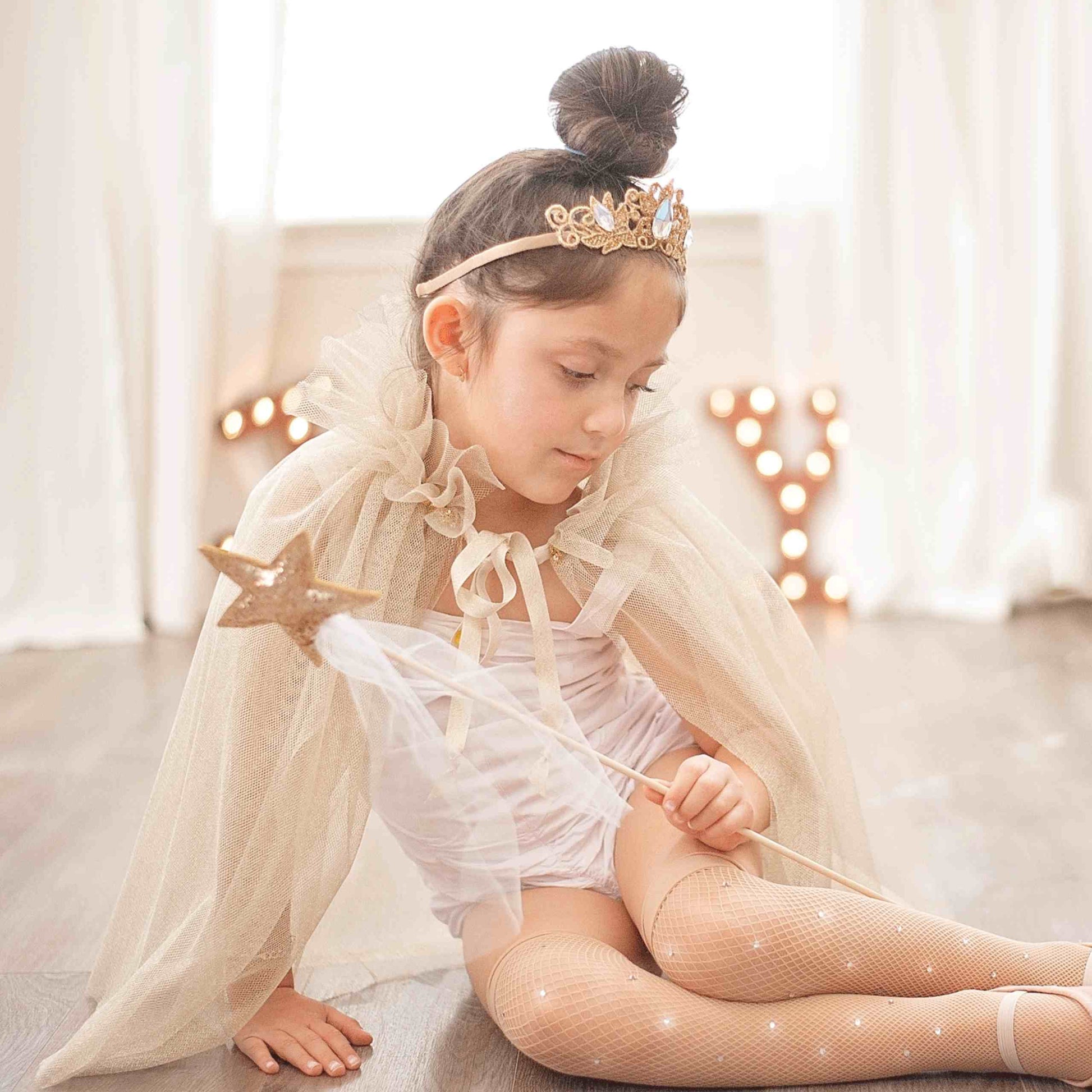 a little girl sitting on the floor wearing a tiara