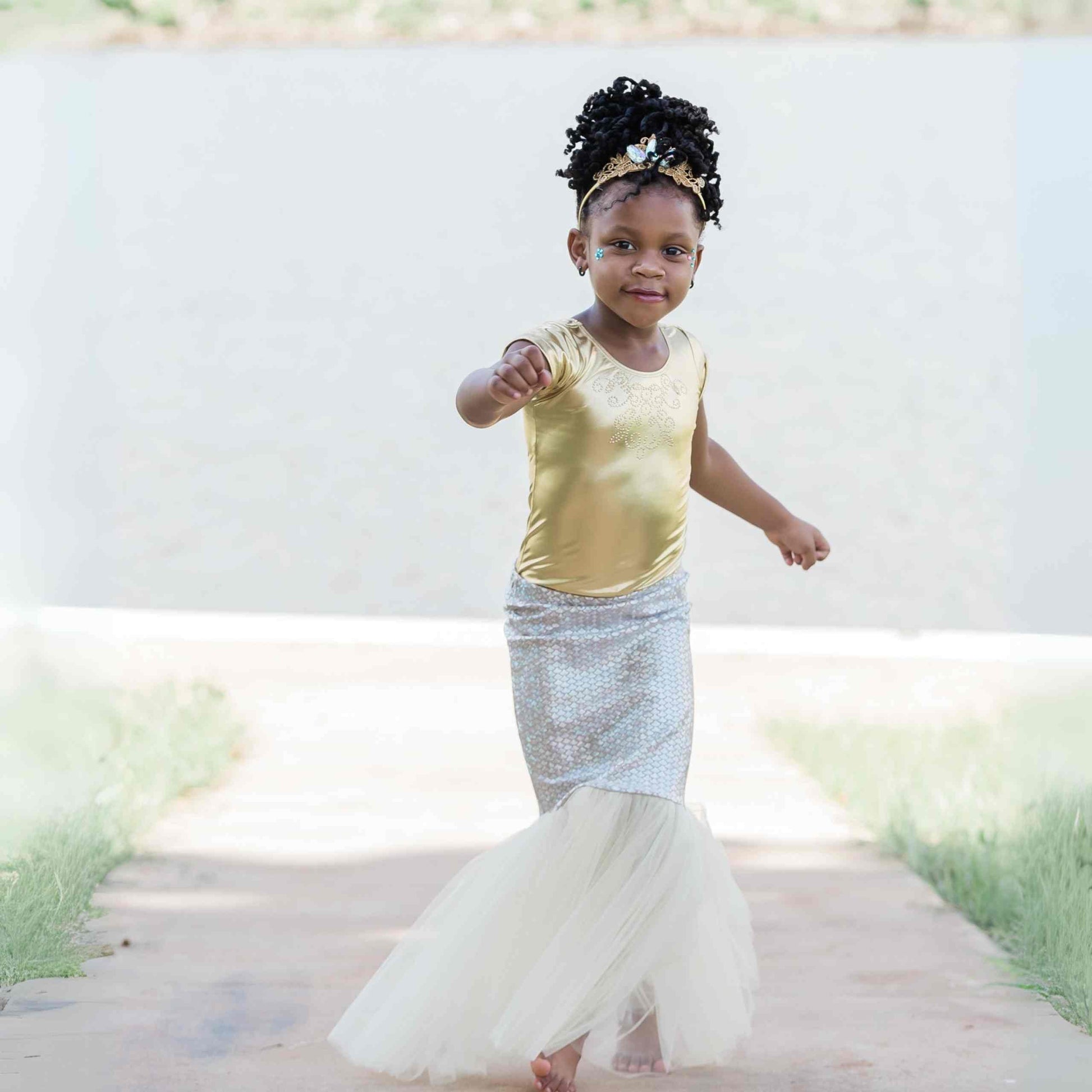 a little girl in a gold shirt and a white skirt