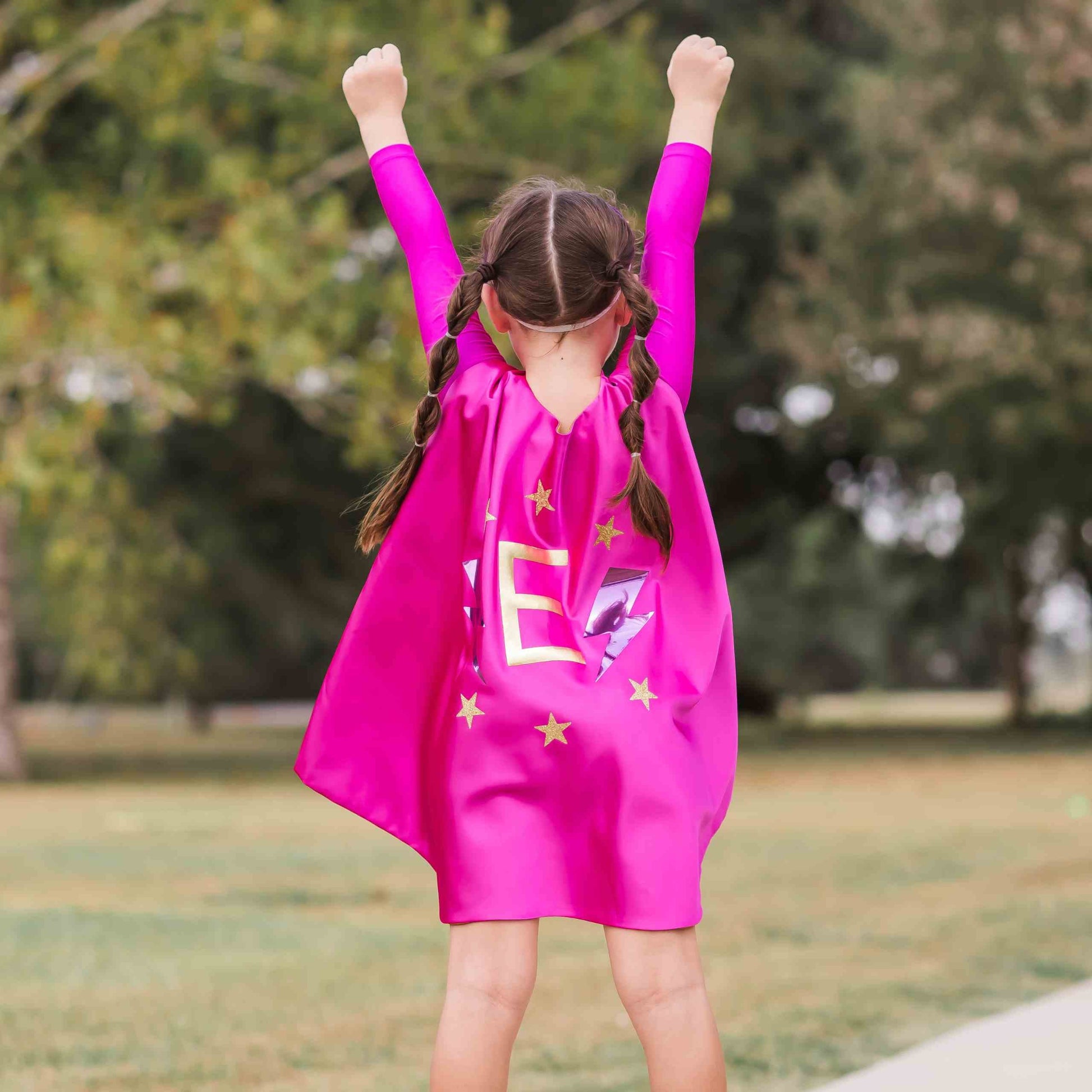 a little girl in a pink cape standing on a skateboard