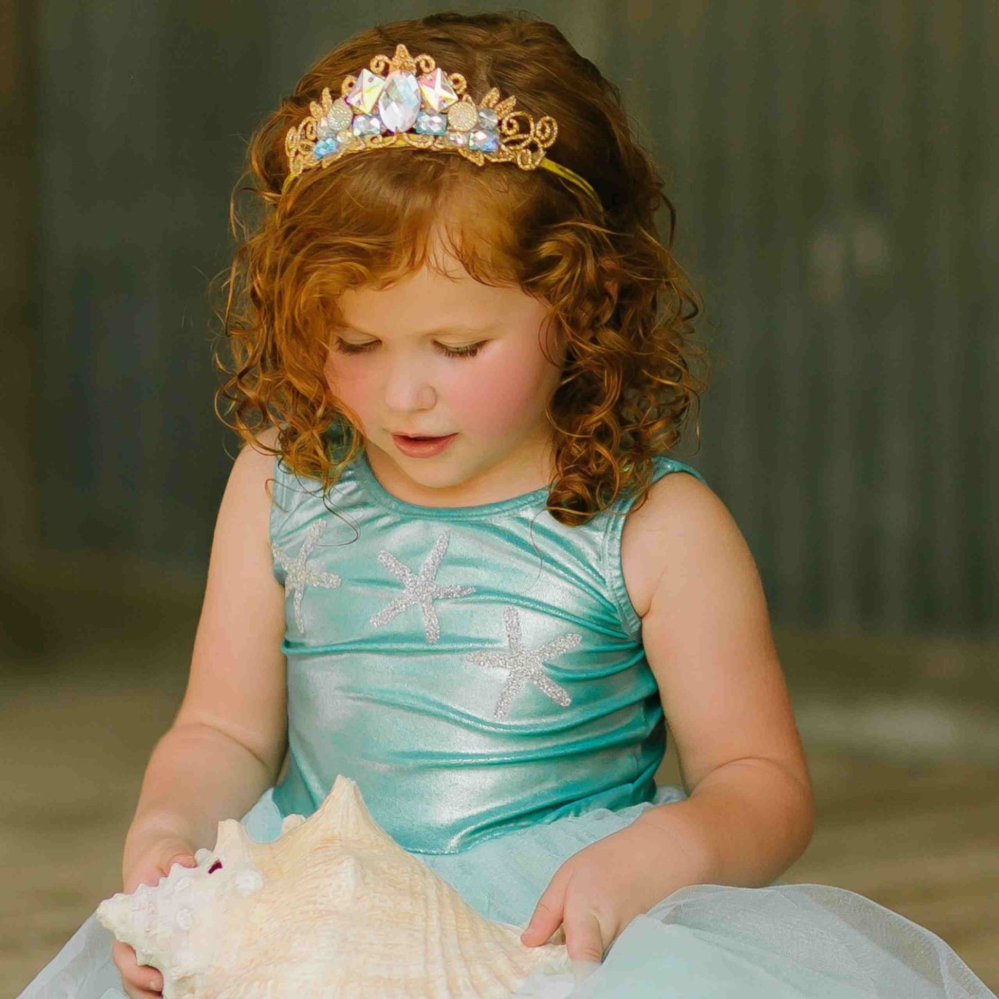 a little girl in a blue dress holding a seashell